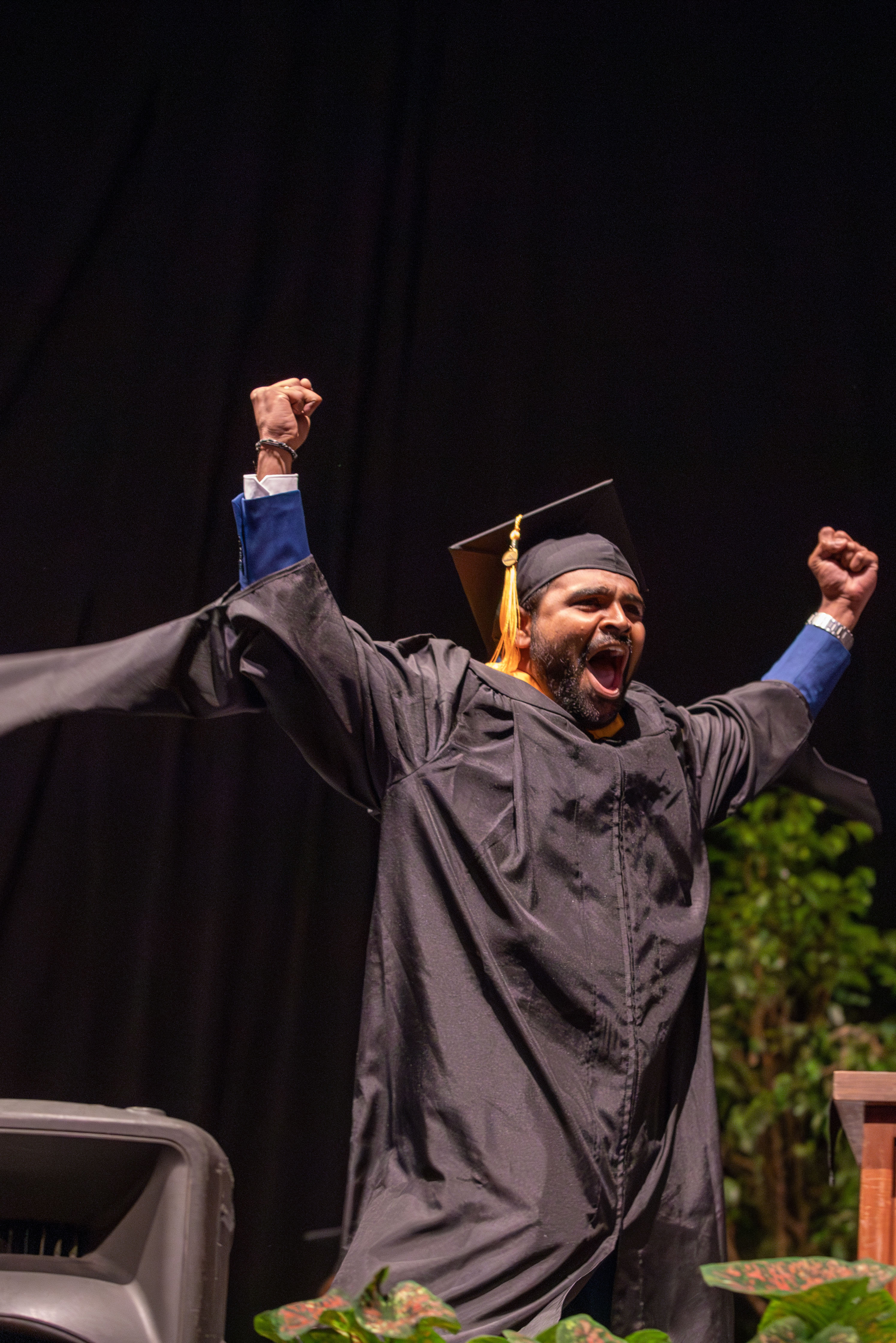 A student wearing graduation regalia points to the sky after receiving his diploma.