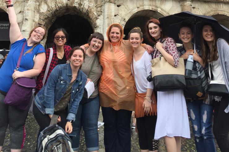 A group of smiling students stand in front of arched architecture overseas.