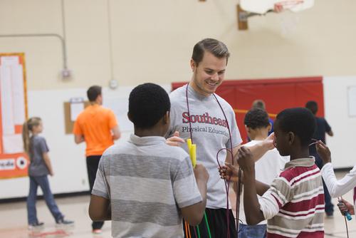 A young man with a jump rope around his neck talks to two children.