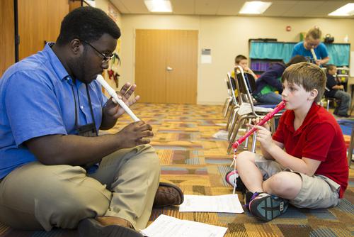Joseph Moore sits on the floor across from a student, teaching him to play a recorder.