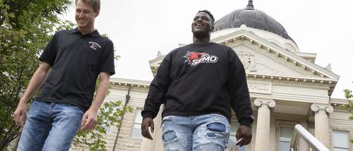 Two students smile while walking near Academic Hall.