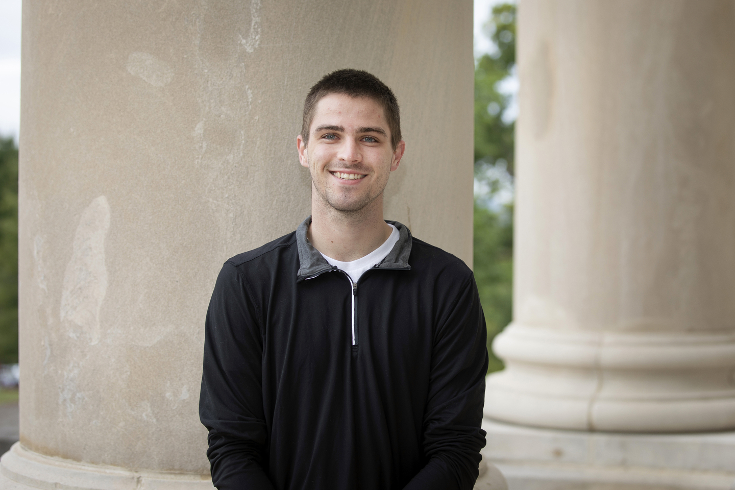 Graduate Student, Andrew Behrmann, stands in front of a pillar at Academic Hall.