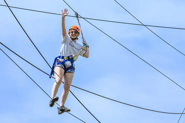 a camp redhawk student stands on the ropes course and waves down at the photographer