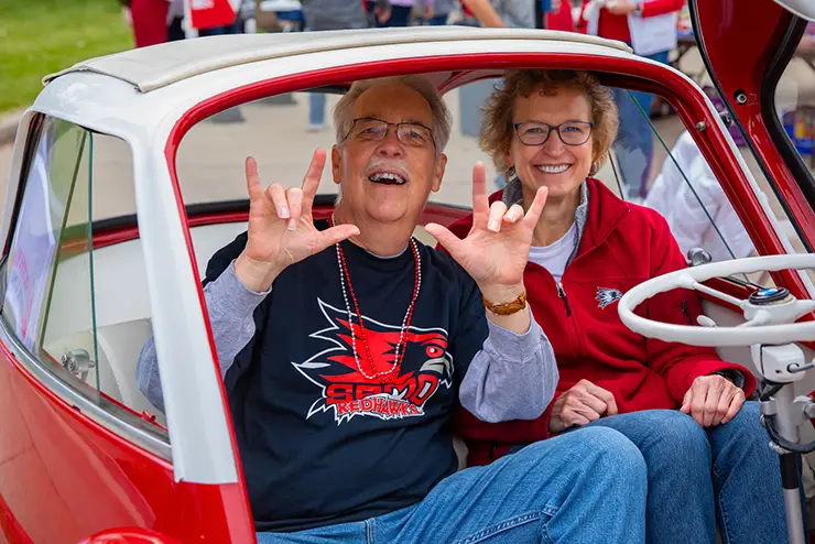two older semo alumni pose for a picture in a tiny car during the homecoming parade