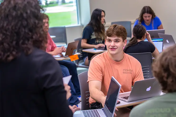 a group of SEMO students on laptops, works together during a class project, one looks up at the approaching instructor