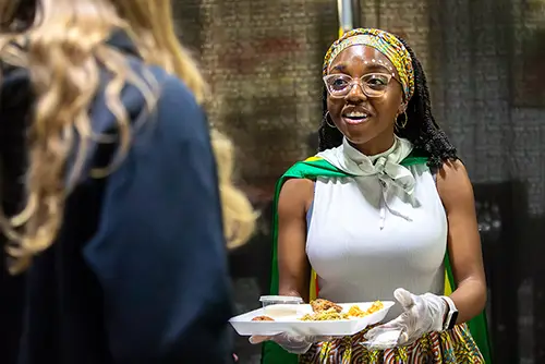 a student working at Carpe Diem serves an attendee a plate of food