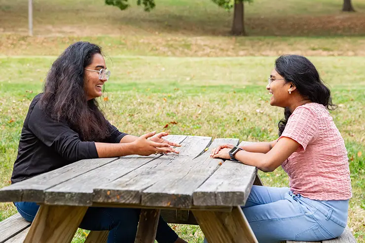 two international students sit together at a picnic table and have a conversation