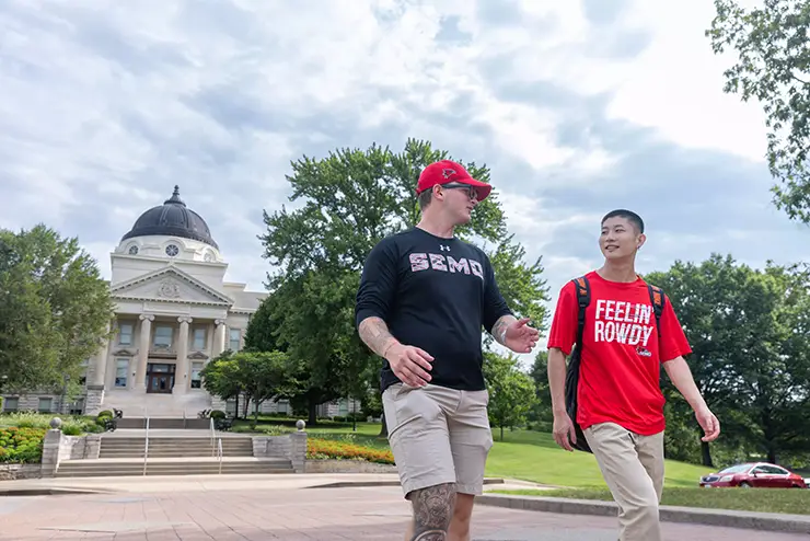 two SEMO students, one international, walk across the street in front of Academic hall
