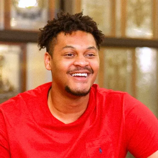 joshua chambers smiles widley wearing a red shirt during an interview