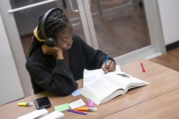 a SEMO student sits at a table with her coursework materials spread out in front of her, listening to headphones while she studies