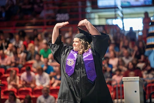 Woman graduating with arms raised in excitement. 