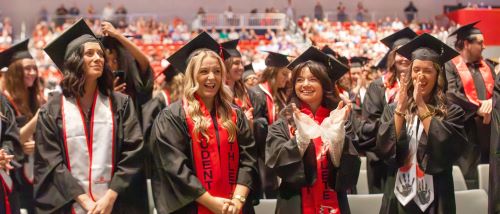 Four graduates cheer during graduation.