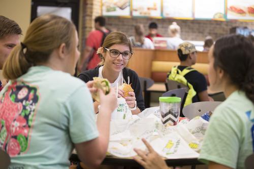 A student smiles while eating with a group at Subway in the Scully Building.