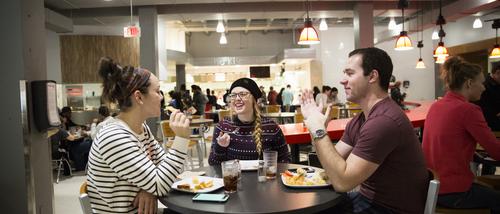 Students smile while sitting at a table and eating at Towers Café.