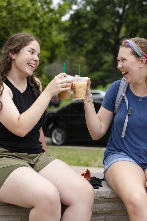 Students clink coffee cups together on the patio outside Starbucks. 