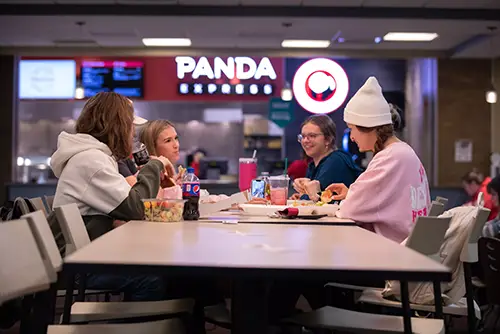 students sit at a table with the panda express sign out of focus in the background behind them