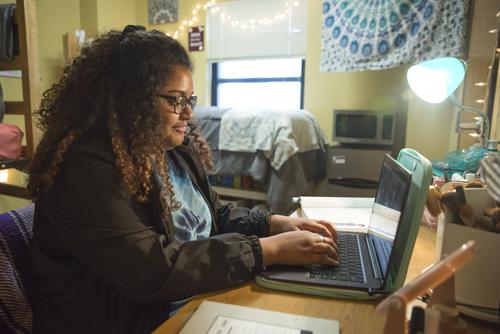 A semo student works on homework on her laptop in her dorm room.  