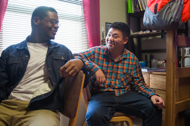 Roommates sit at their desks and smile as they laugh while hanging out in their dorm room.
