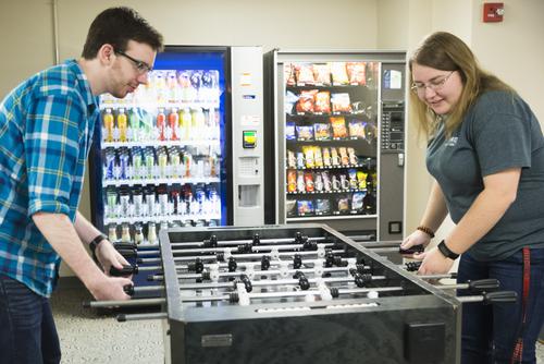 Two students play foosball in the game room, which houses two vending machines. 