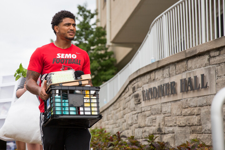 A student wearing a SEMO Football shirt, carries belongings to a room in Vandiver Hall.