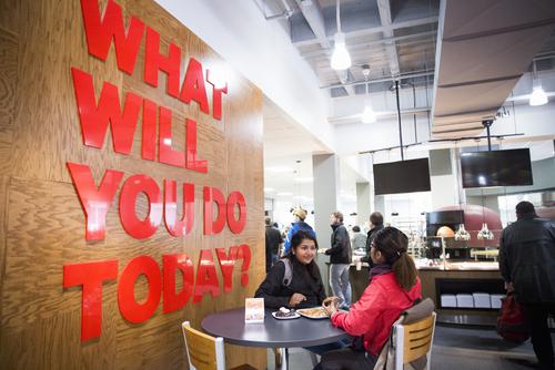 Students catch up while dining at Towers Café next to a wall that reads “What will you do today?”  
