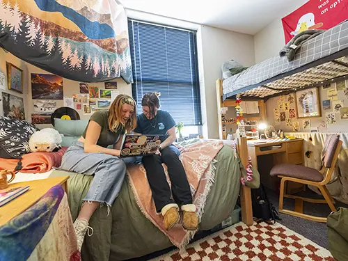 two roommates in one of SEMO's residence halls sit together on a bed looking at a computer screen and laughing