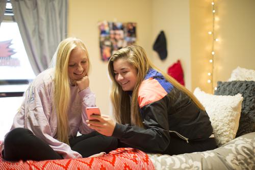 Roommates smile as they watch a video on their phone in their Towers North room. 