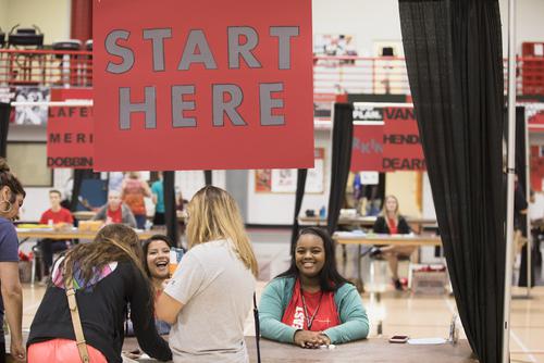 Volunteers sitting at a table with a “start here” sign help with check-in on Move-in day. 