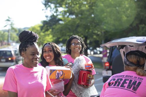 The move-in day crew helps carry a new student’s belongings from a car to <a href=