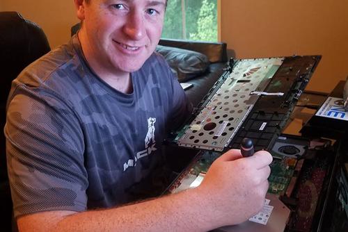 Southeast Alumnus, Cory Brethold, sits at a desk working to repair a part from a laptop.