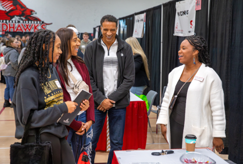  Two students and two adults stand around a table talking on Show Me Day