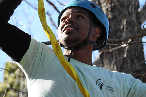 a student wearing safety gear prepares to climb a rope course