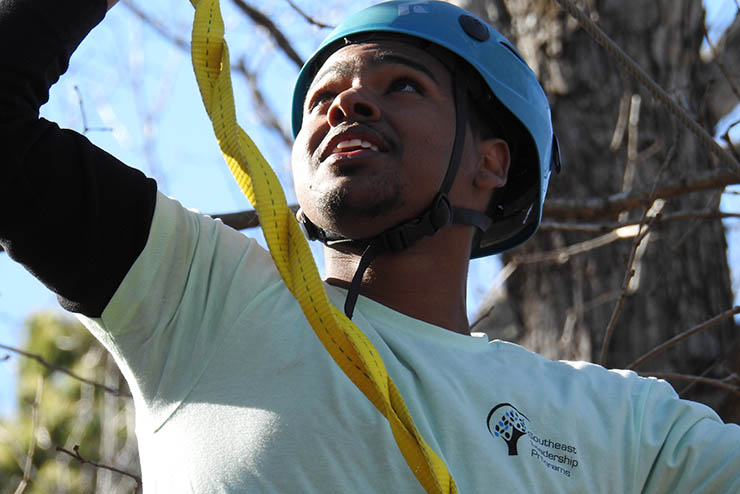 a student wearing safety gear prepares to climb a rope course