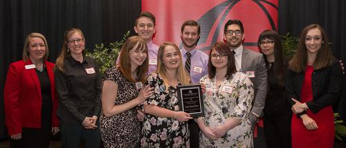  A group of students holding their Student Life and Leadership Award plaques stand with their professors. 