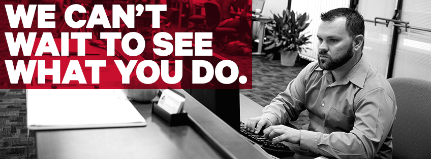 shot in black and white, a student sits at a computer working, text overlay of "We can't wait to see what you do."