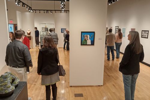 People walk around an art exhibit for high school student's works.