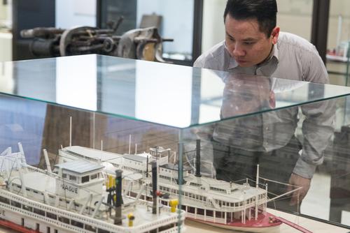 An individual bends down to look into a glass case displaying a pair of riverboat models. 