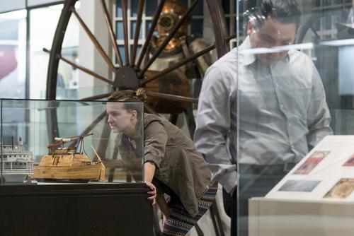 A young woman leans down to look into a glass case displaying boat models. 