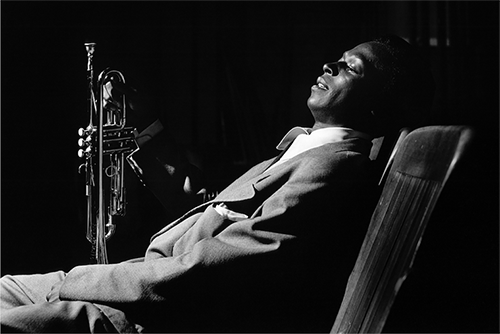 A Miles Davis black and white photograph of him reclining with a saxaphone.