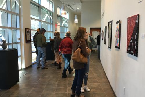 Groups of museum visitors stand in the front hallway of the museum talking and viewing artwork