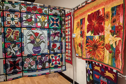 colorful handmade quilts hanging up in a gallery for viewing