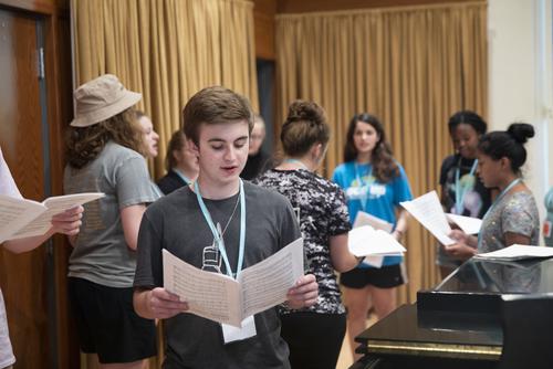 A group of teenagers attending the Vocal Arts class practice singing with sheet music.