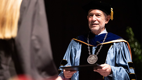 Image of Southeast President Dr. Carlos Vargas handing a diploma to a graduating student at commencement.