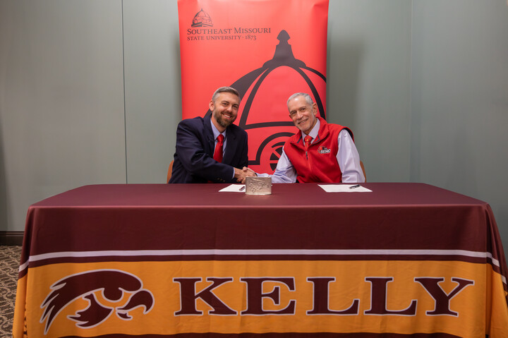 Scott County RIV superintendent Dr. Bradley Kolwyck shakes hands with SEMO president Carlos Vargas at a signing in front of a red banner.