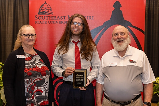 A student is presented with a black plaque award in front of a red banner.