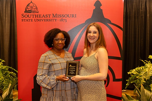 A student is presented with a black plaque award in front of a red banner.