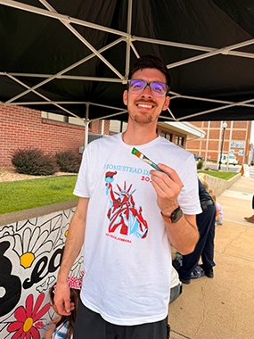A young man smiles at an outdoor community event. 