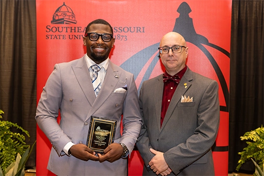 A student is presented with a black plaque award in front of a red banner.