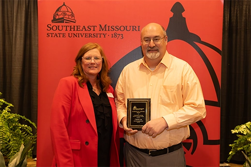 A student is presented with a black plaque award in front of a red banner.
