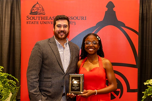 A student is presented with a black plaque award in front of a red banner.